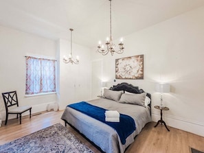 A bedroom with a bed, a chandelier, a window with curtains, a chair, and a painting on the wall. - 406 Canyon Rd #2 (Ogden)