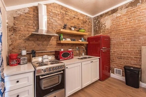 A compact kitchen with a brick wall, a red refrigerator, a microwave, a stove, and white cabinets. - 406 Canyon Rd #2 (Ogden)