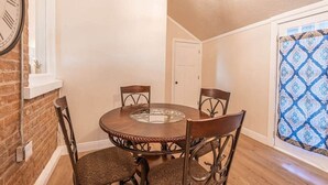 Un coin repas avec une table ronde et des chaises, une horloge au mur et un rideau à motifs.