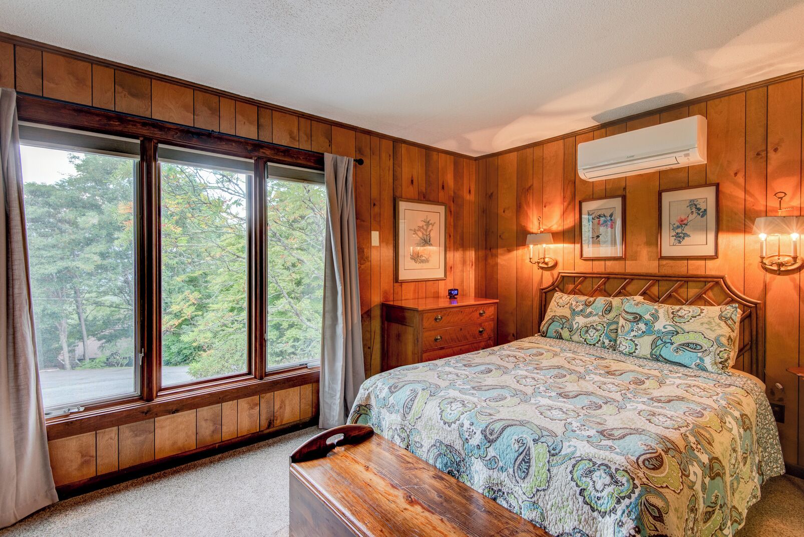 A wooden-paneled bedroom with a bed, a nightstand, a dresser, and a window with curtains.