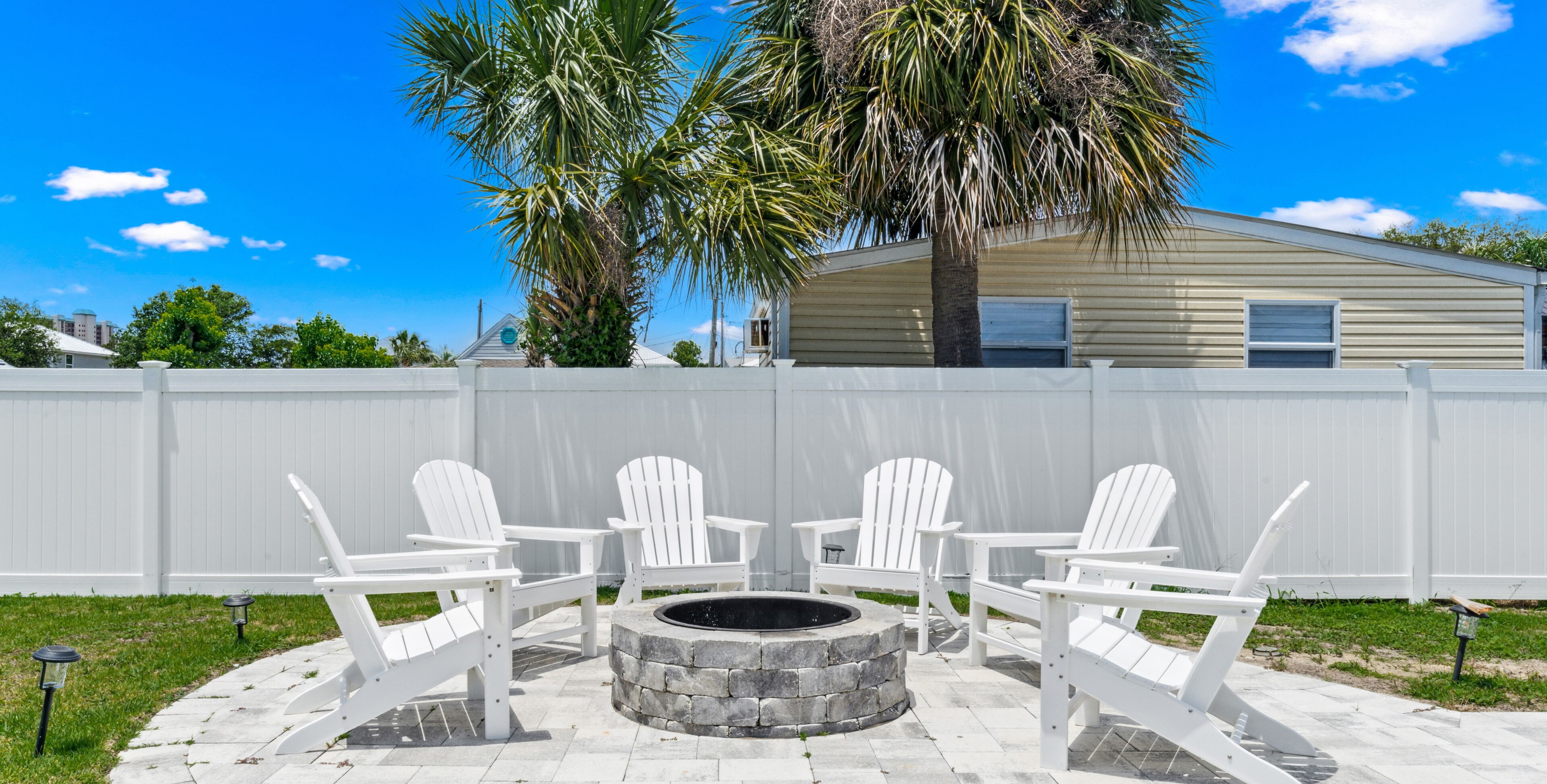A patio with four white Adirondack chairs and a stone fire pit.