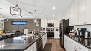 A modern kitchen with white cabinets, stainless steel appliances, a granite countertop, and pendant lighting. - Raven's Nest - Mins to Beach Heated Pool & Pet Friendly (Panama City Beach)