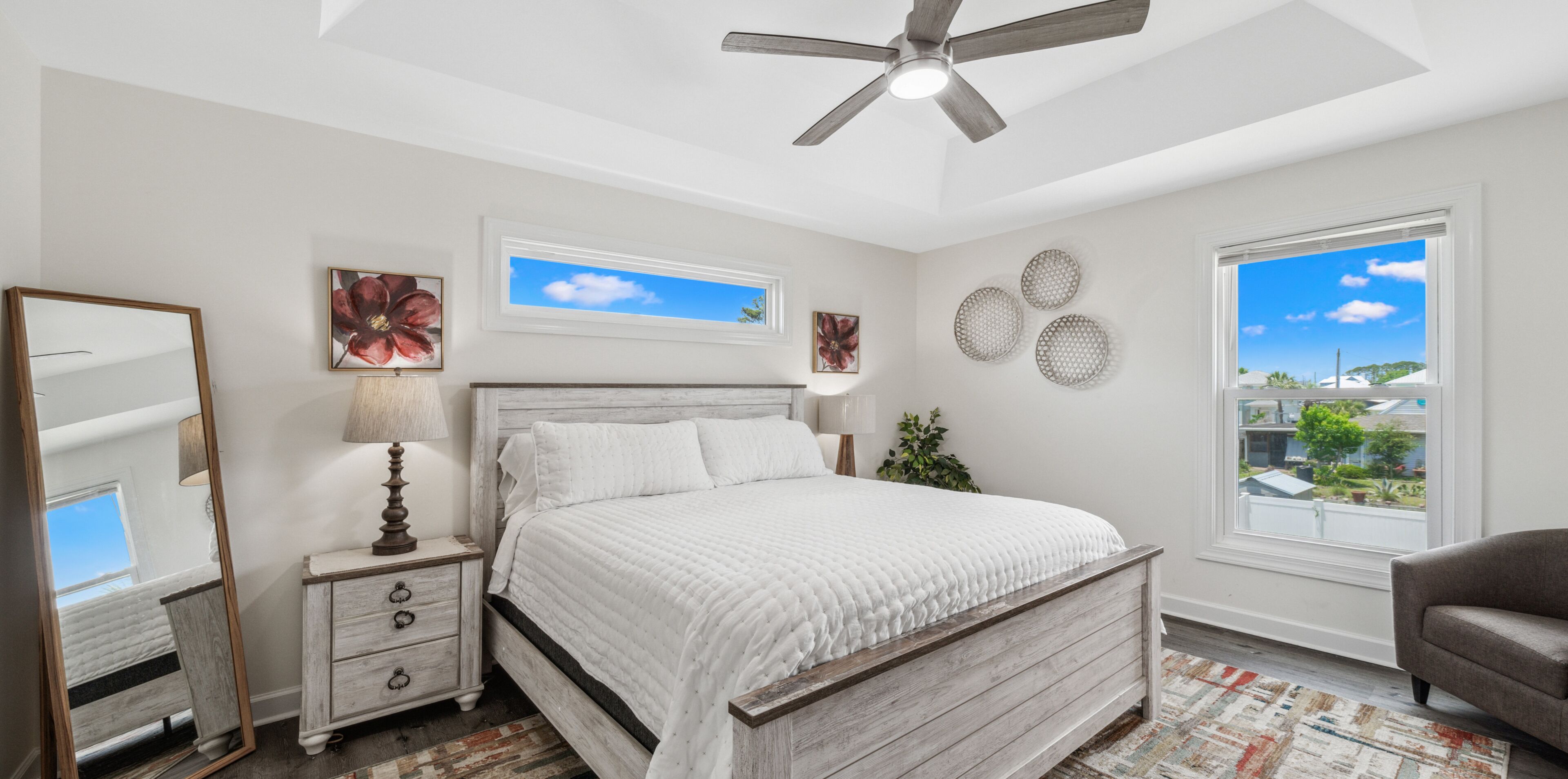 A bedroom with a bed, a ceiling fan, a window with a view, and wall art.