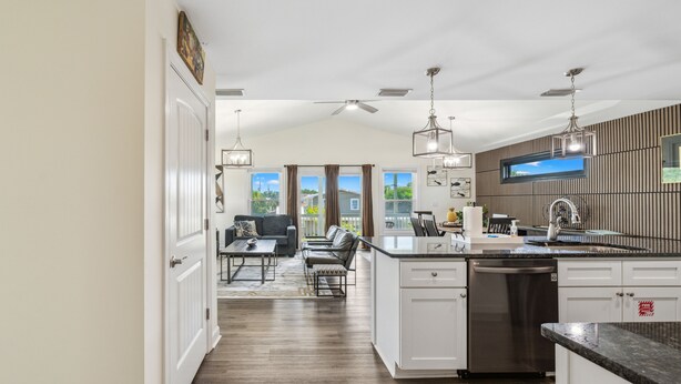 A modern kitchen with white cabinetry, an island with a sink, and a dining area with a table and chairs. - Raven's Nest - Mins to Beach Heated Pool & Pet Friendly (Panama City Beach)