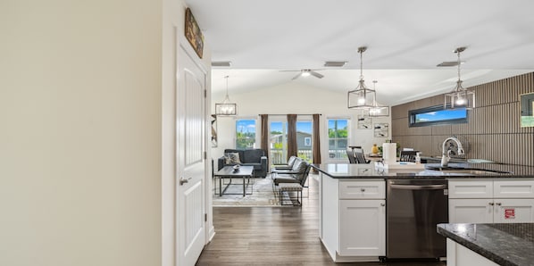 A modern kitchen with an island, white cabinetry, and a dining area with a sofa and table. - Raven's Nest - Mins to Beach Heated Pool & Pet Friendly (Panama City Beach)