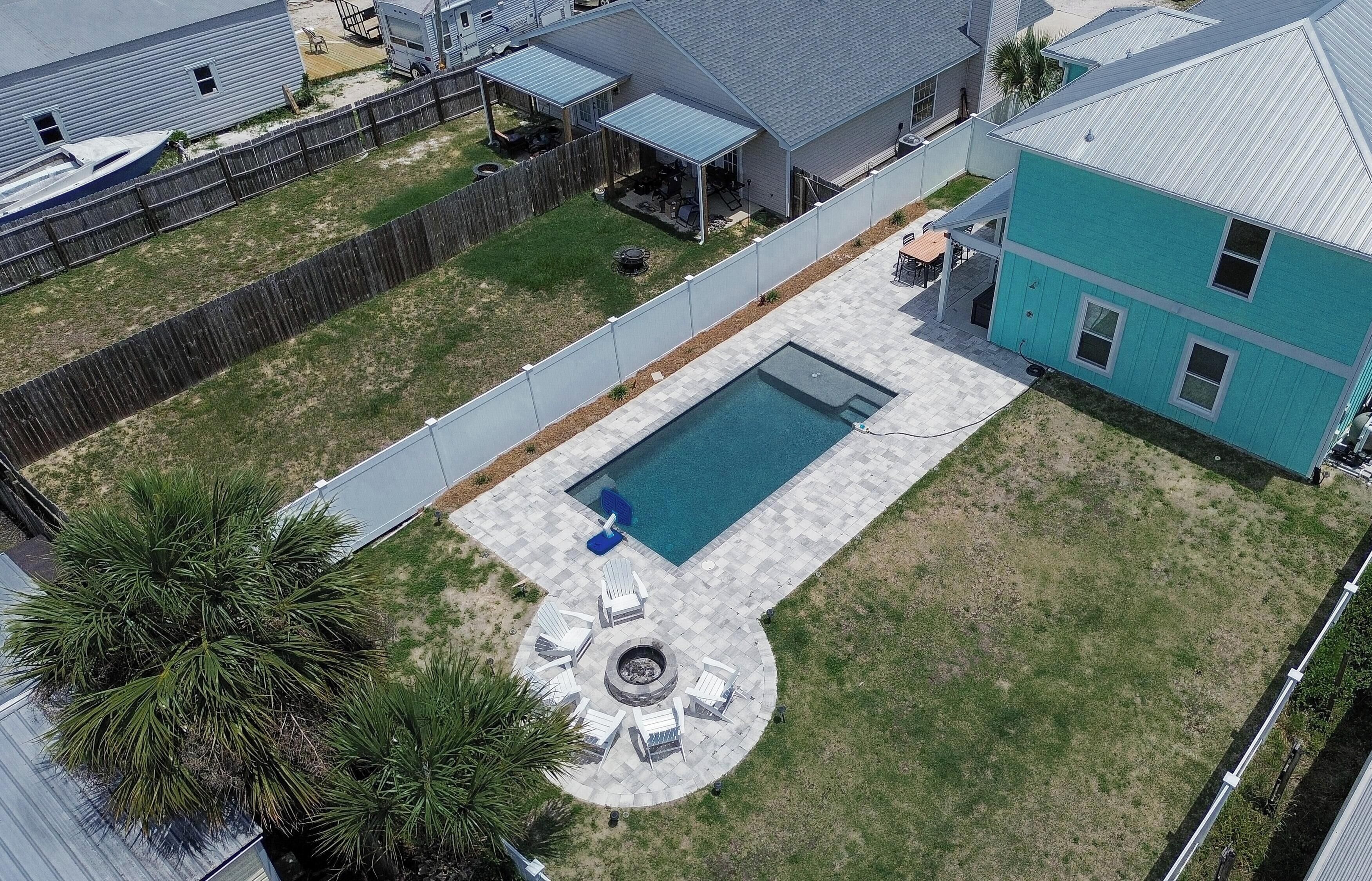 Un patio trasero residencial con piscina, un área de patio cercada y una casa de fachada azul.