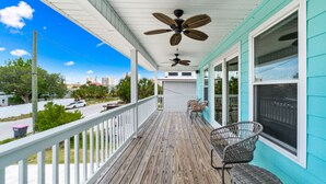 A wooden deck with a ceiling fan, wicker chairs, and a view of the street and buildings. - Raven's Nest - Mins to Beach Heated Pool & Pet Friendly (Panama City Beach)