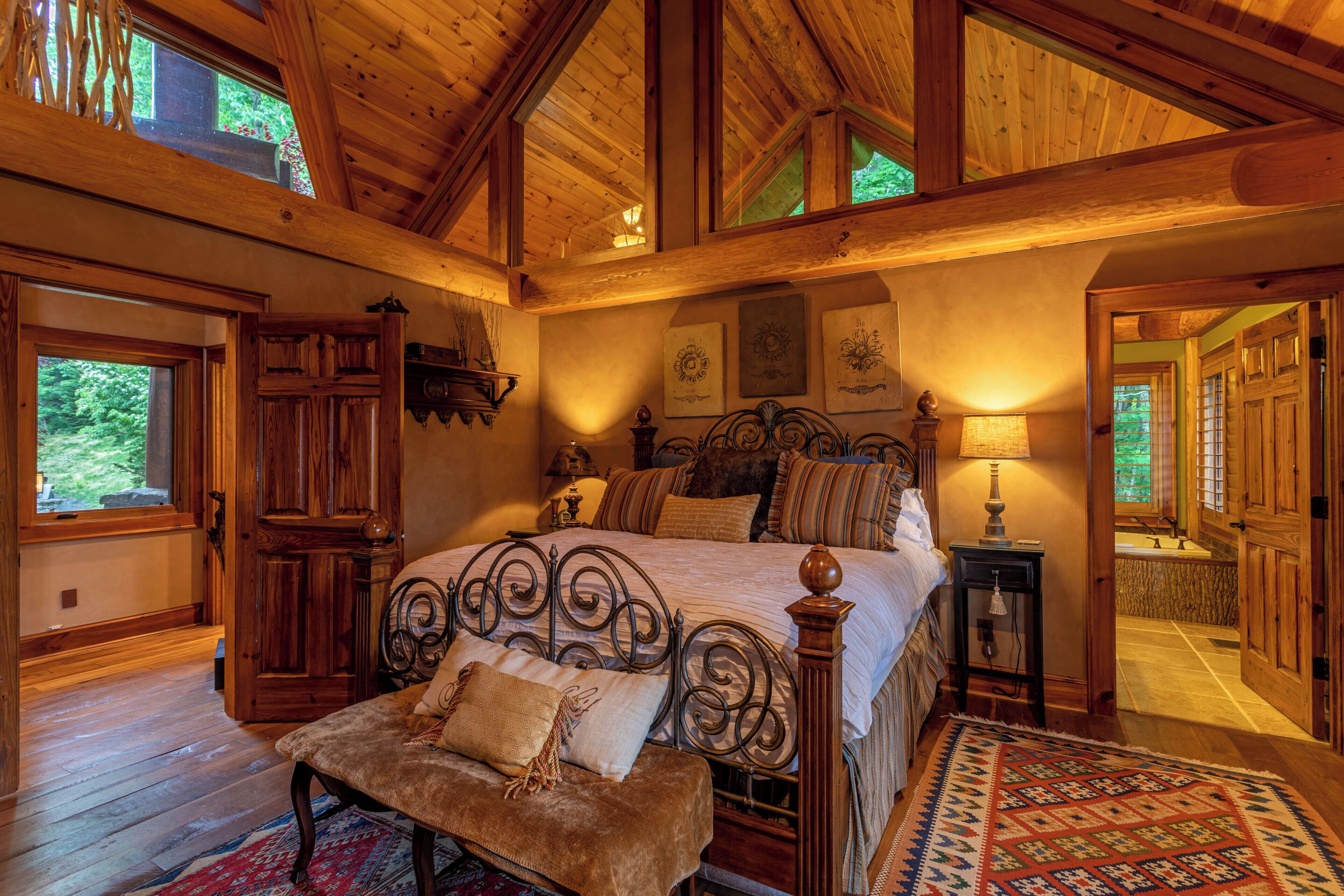 A spacious bedroom with a large bed, wooden ceiling beams, and a view of the outdoors.