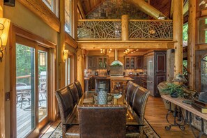 A spacious dining area with a high ceiling and exposed wooden beams, a central island with a sink, and leather-upholstered chairs. - Big Bear Lodge at Eagles Nest (Banner Elk)
