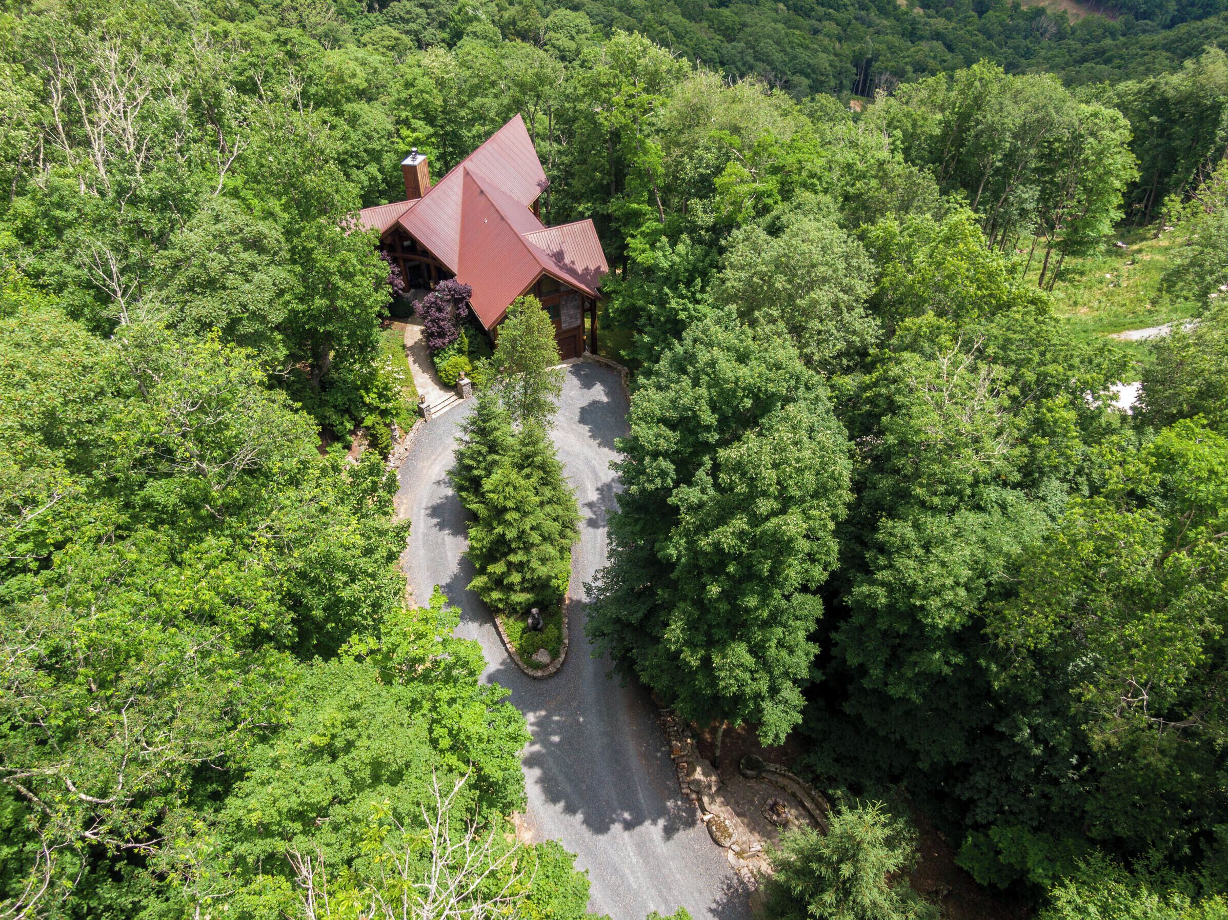 An aerial view of a lodge surrounded by dense forest, with a winding road leading to the entrance.