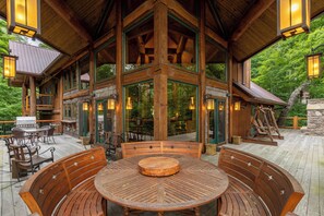 A wooden deck with a round table and benches, surrounded by glass doors and windows, overlooking a forested area. - Big Bear Lodge at Eagles Nest (Banner Elk)