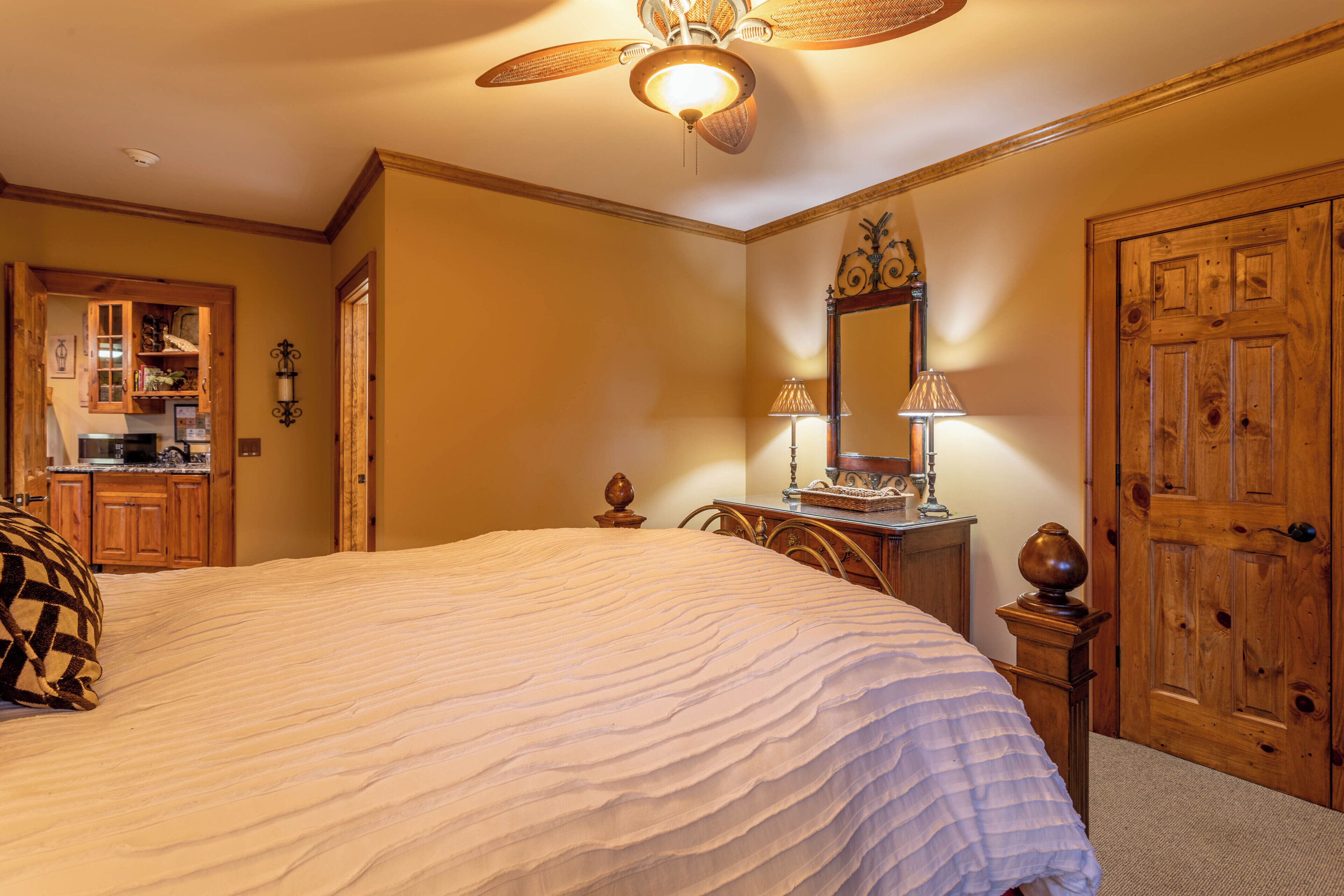 Une chambre avec un grand lit, une armoire en bois et un ventilateur de plafond.