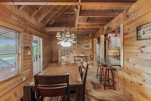 A wooden cabin interior with a dining area, kitchen, and a staircase leading to the upper floor. - The Great Bear Lodge (Vilas)
