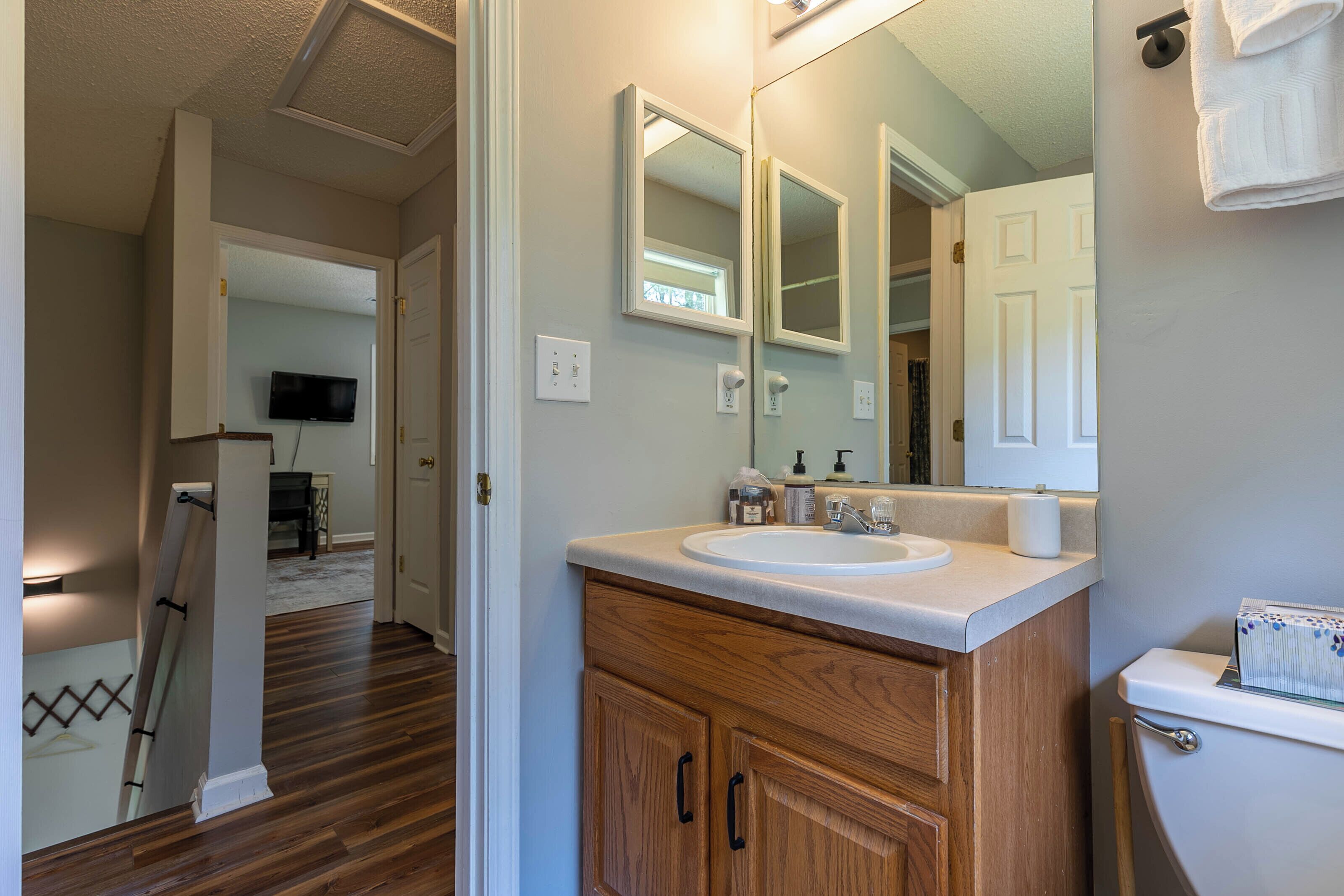 A bathroom with a wooden vanity, a sink, and a toilet. There is a mirror above the sink and a towel hanging on the wall.