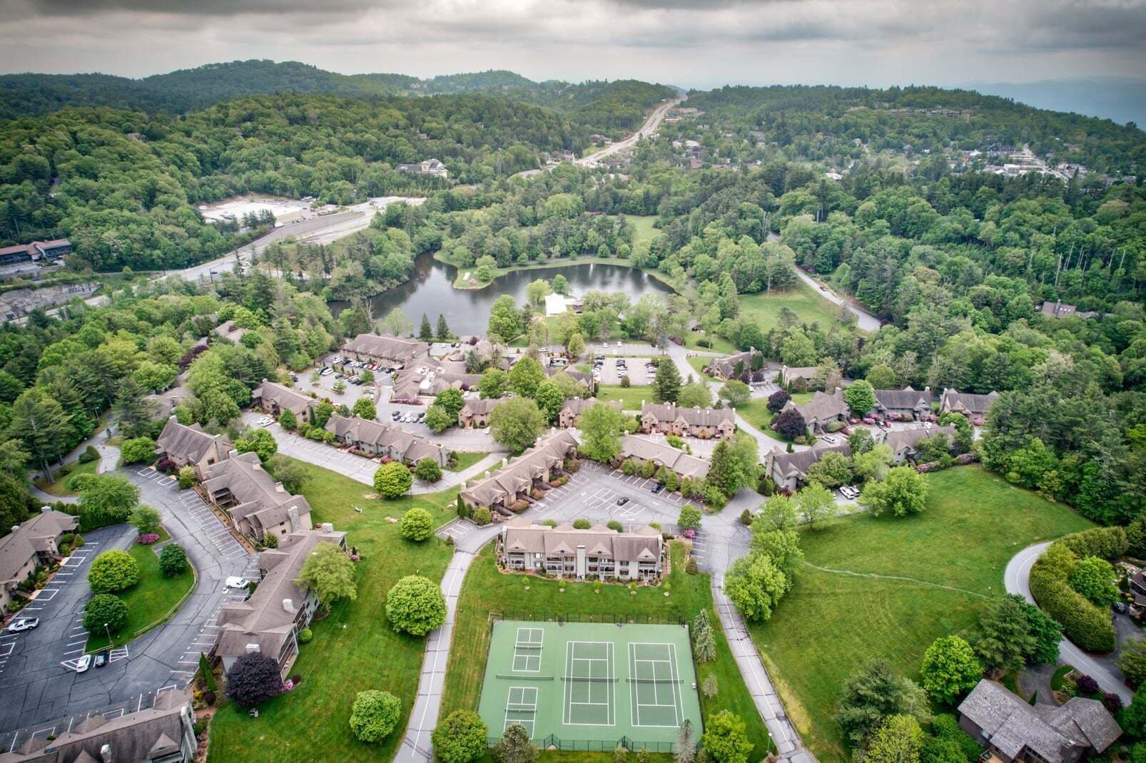 An aerial view of a residential area with houses, a tennis court, and a lake.