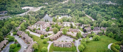 An aerial view of a residential area with houses, a tennis court, and a lake.
