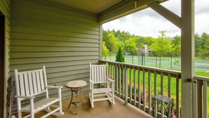 Een veranda met twee witte Adirondack-stoelen en een klein rond tafeltje.
