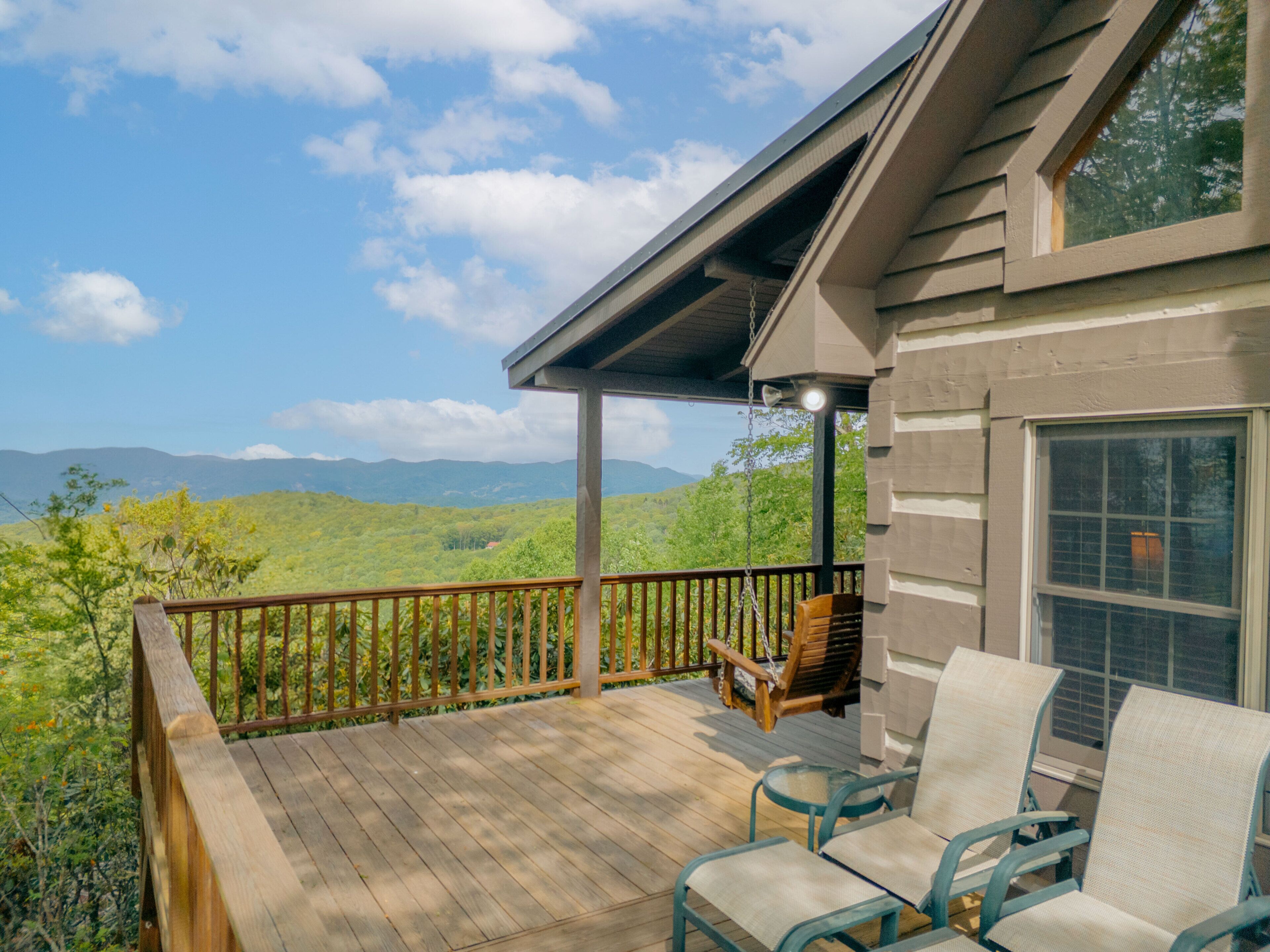A wooden deck with outdoor furniture, a railing, and a view of green hills and mountains.