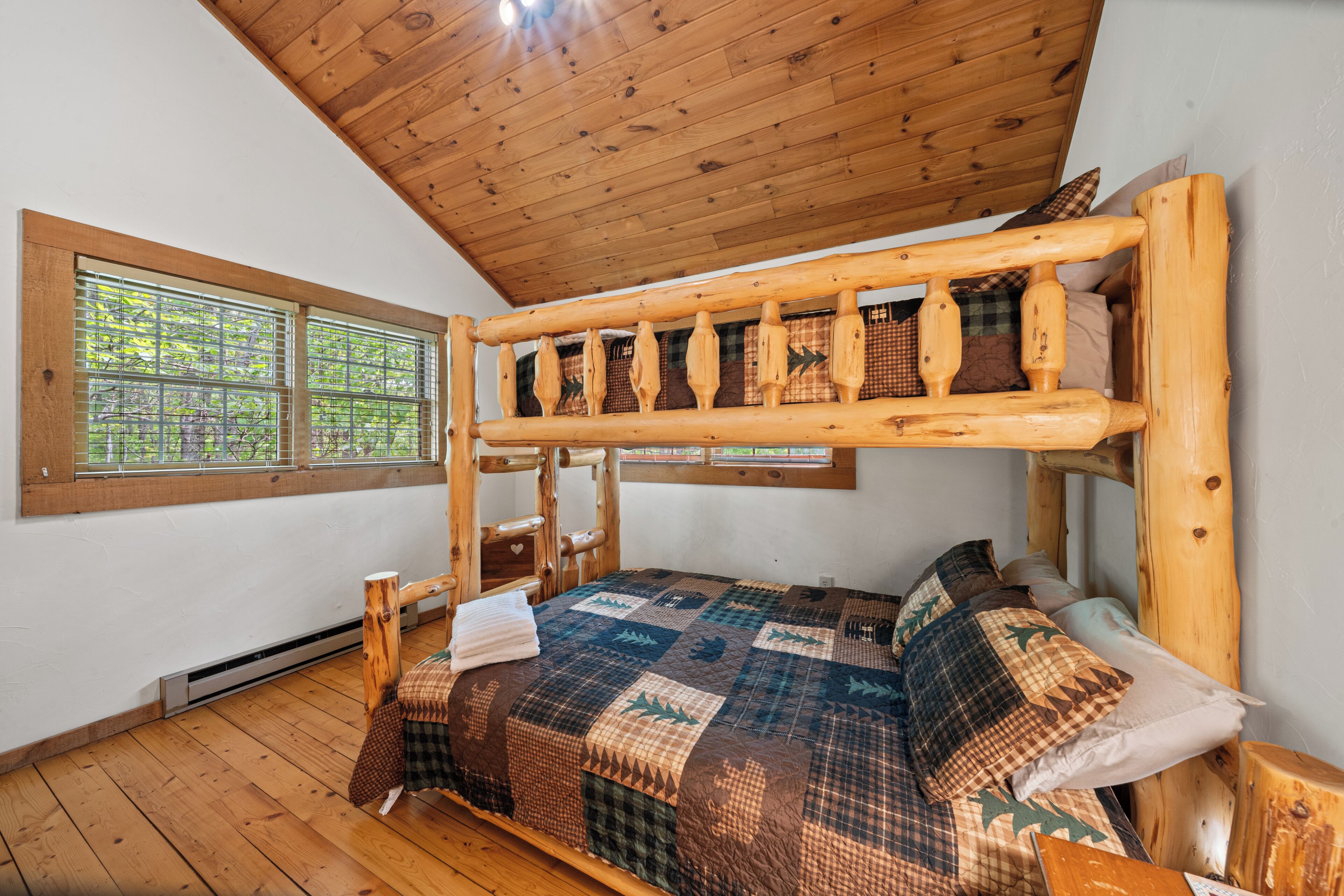 A bunk bed with a wooden headboard, a quilted bedspread, and a window with a view of trees.