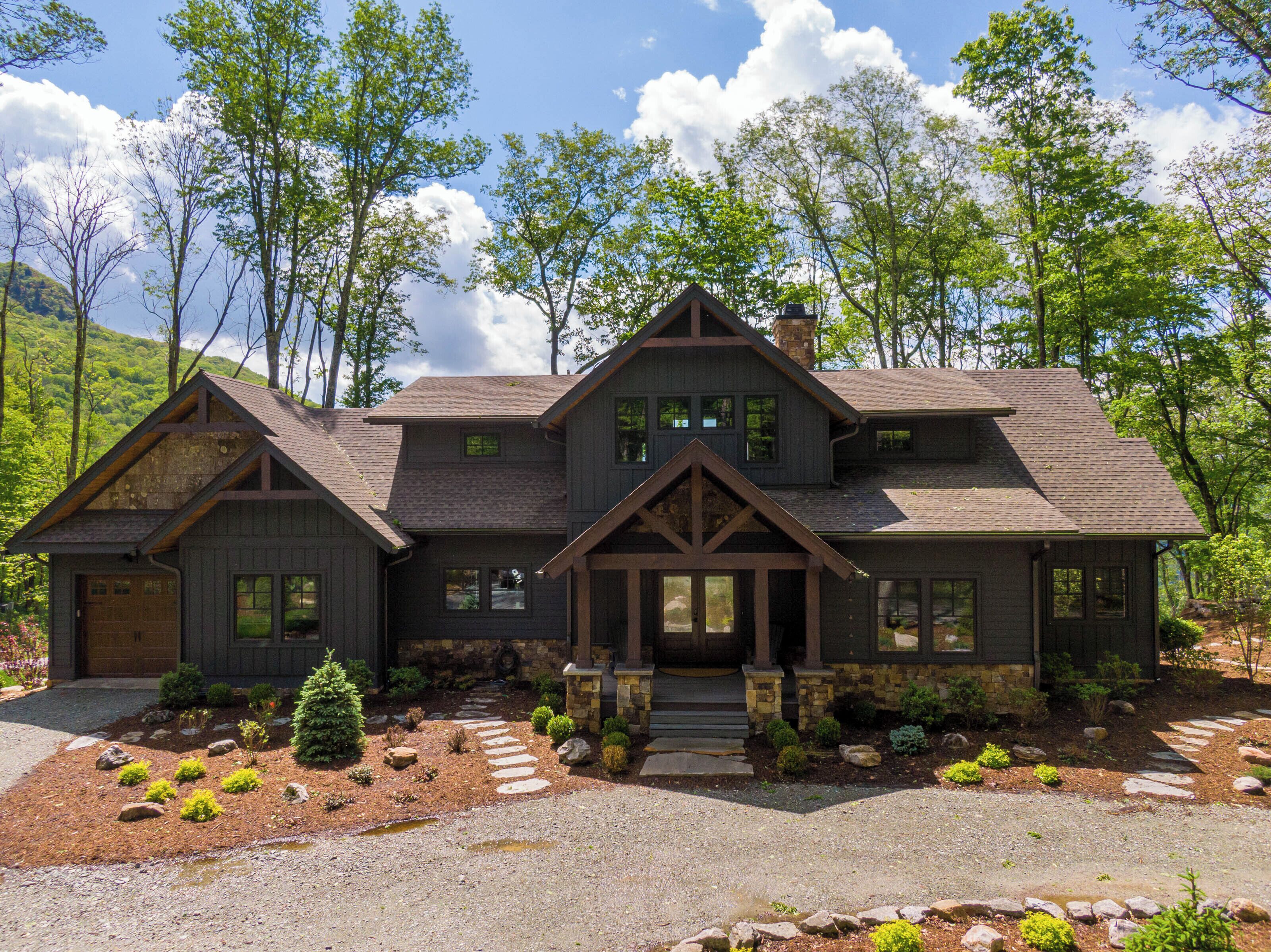 A two-story house with a stone foundation, a large front porch, and a landscaped front yard with stepping stones and small shrubs.