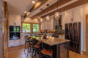 A spacious kitchen with a large island, stainless steel appliances, and a rustic wooden ceiling. - Howling at the Moon at Eagles Nest (Banner Elk)