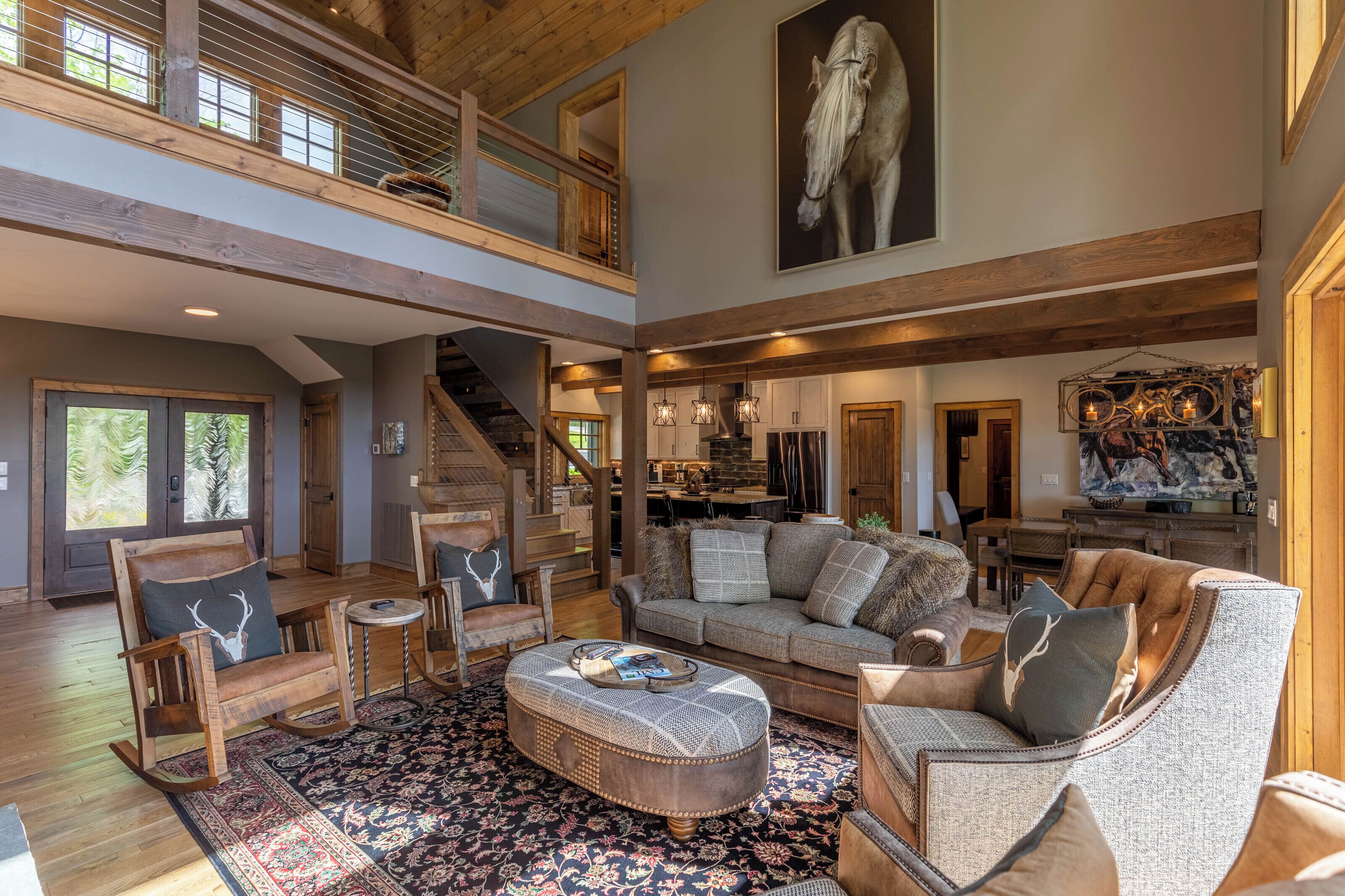 Un vaste espace de vie doté d’un haut plafond, de poutres en bois, d’un grand tableau représentant un cheval et d’un coin salon confortable comprenant un canapé, des fauteuils et une table basse.
