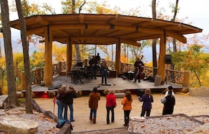 A wooden gazebo with a stage, surrounded by trees and a view of the mountains. - Howling at the Moon at Eagles Nest (Banner Elk)