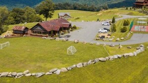 A rural property with a large open field, several buildings, a parking area, and a view of distant mountains. - Howling at the Moon at Eagles Nest (Banner Elk)