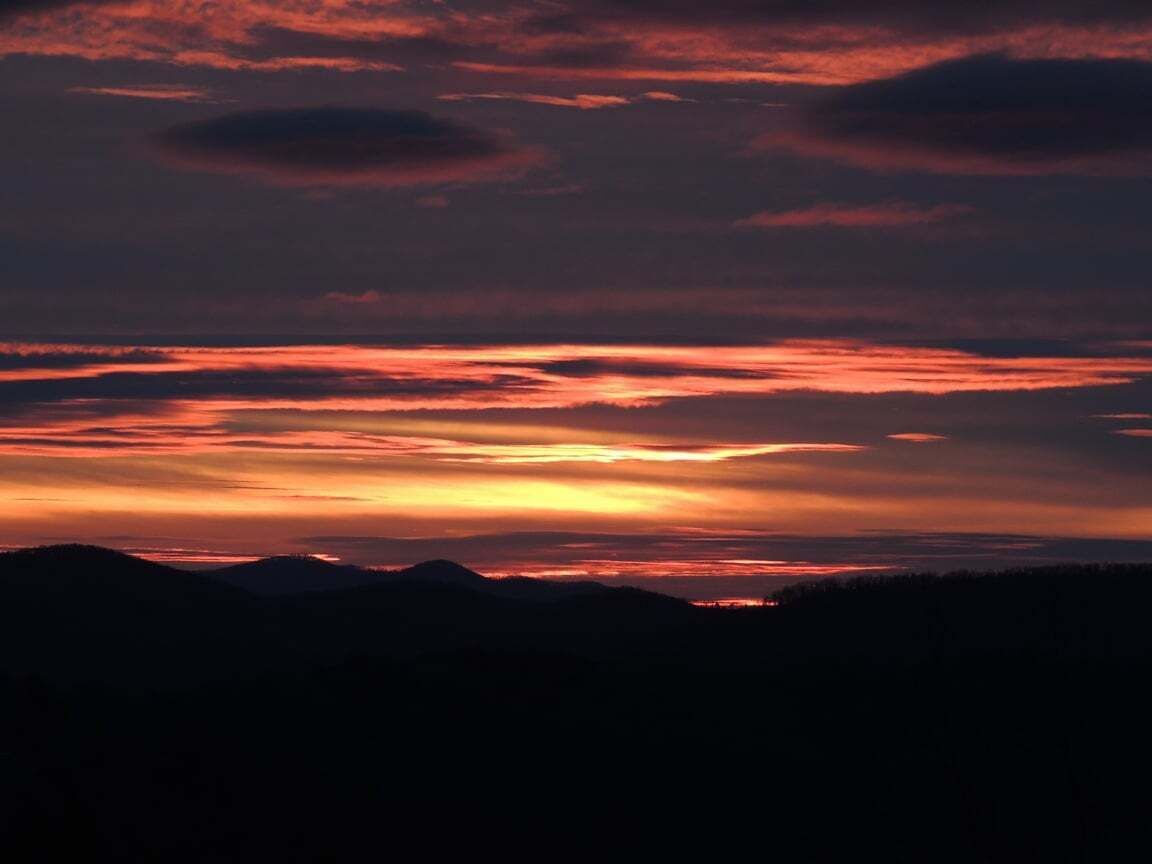 A sunset over a mountainous landscape with silhouettes of hills.