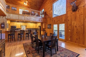 Una cabaña de madera espaciosa con comedor, cocina y balcón.