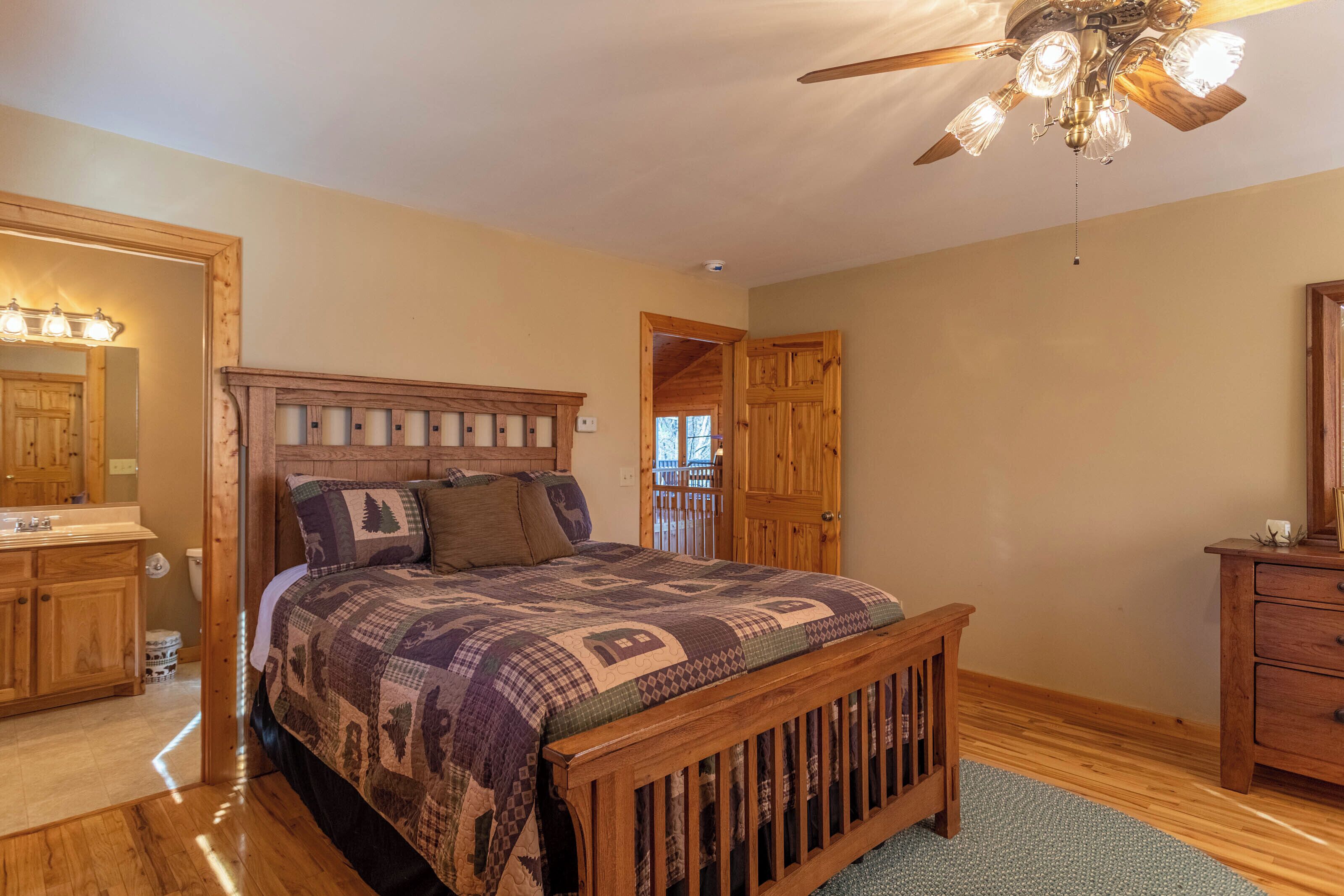Een slaapkamer met een houten bed, een plafondventilator, een houten dressoir en een badkamer met een houten wastafel en wasbak.