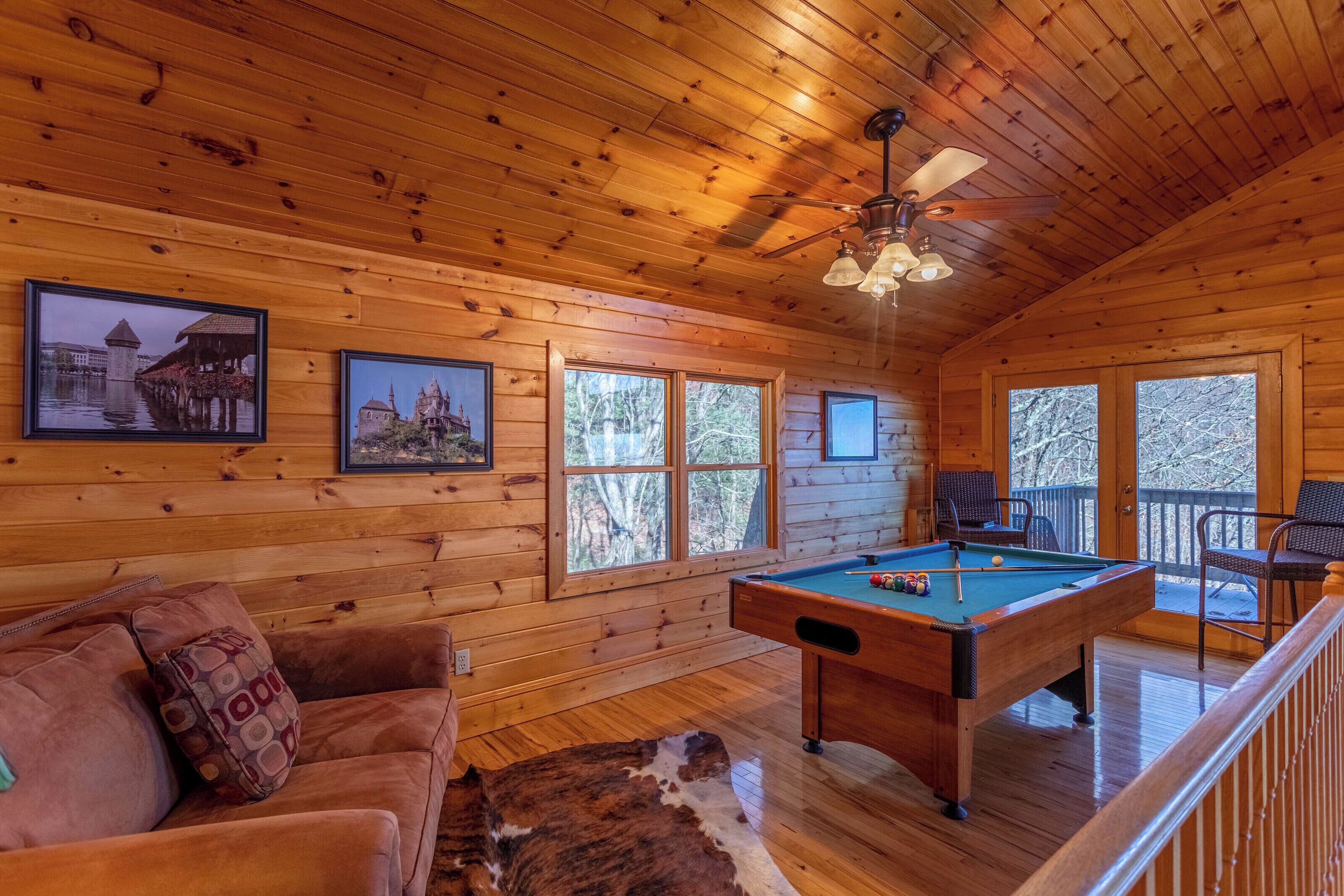 A wooden cabin interior with a pool table, a sofa, and framed pictures on the walls.