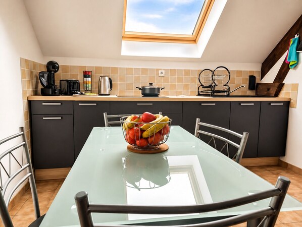 A modern kitchen with a skylight, a dining table with chairs, and a fruit bowl on the table.