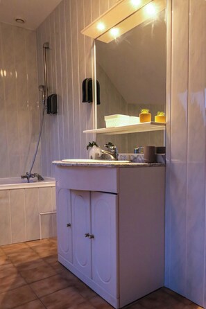 A bathroom with a bathtub, a sink with a mirror, and a shower.