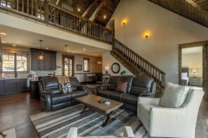 A spacious living area with a high ceiling, a staircase, and a kitchen in the background. - Grayling Lodge at Eagles Nest (Banner Elk)