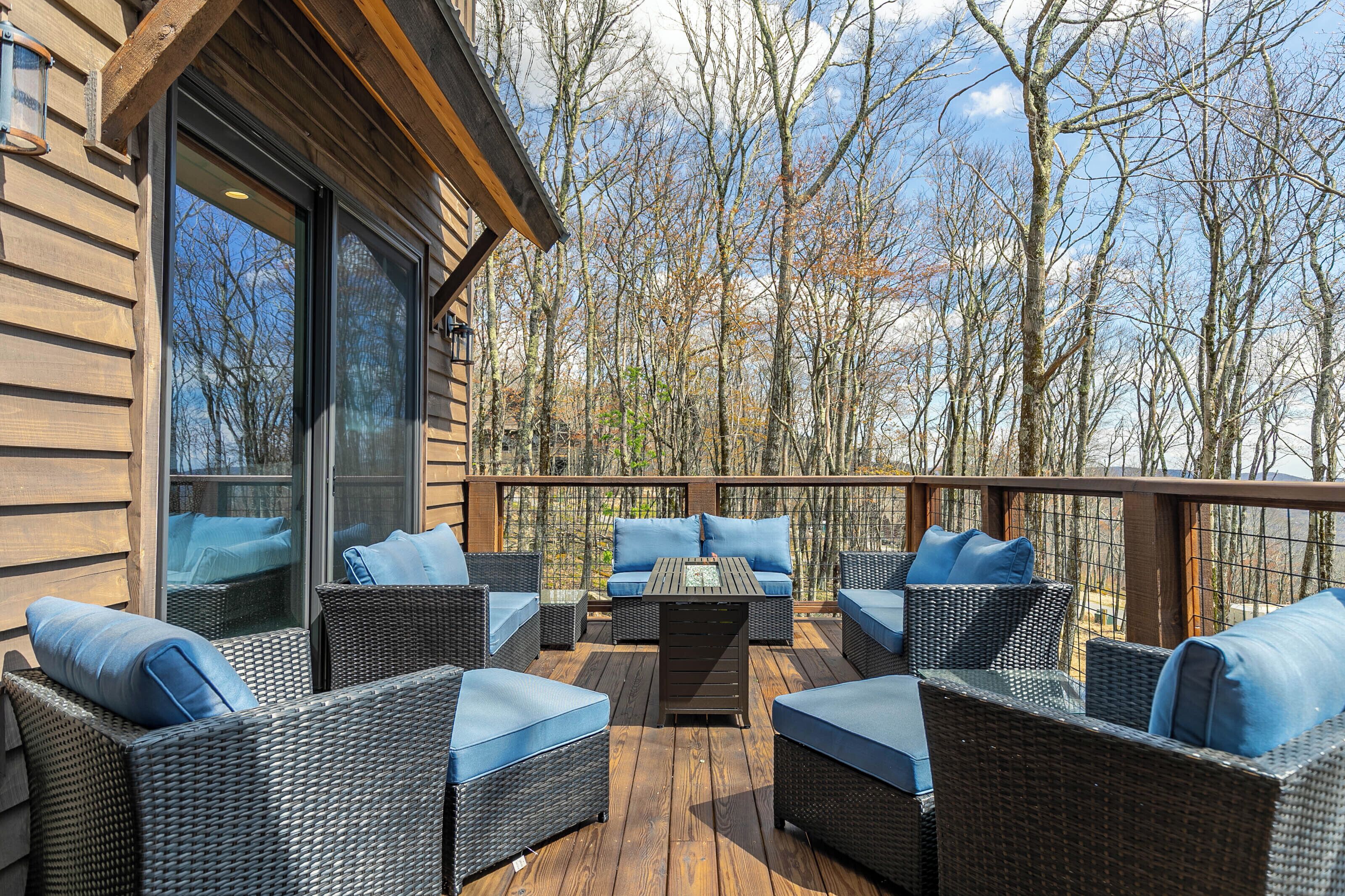 A wooden deck with wicker furniture and blue cushions, overlooking a forested area.