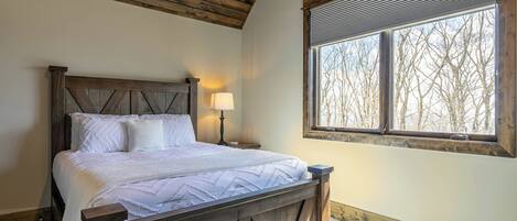 A bedroom with a wooden bed, a nightstand, a lamp, and a window with a view of trees.