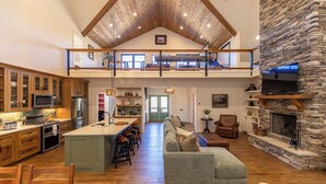 Amplio espacio tipo loft con techo alto, chimenea de piedra, cocina equipada con electrodomésticos modernos y una zona de estar acogedora.