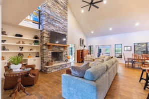 A spacious living room with a stone fireplace, a large sectional sofa, and a dining area with wooden furniture.
