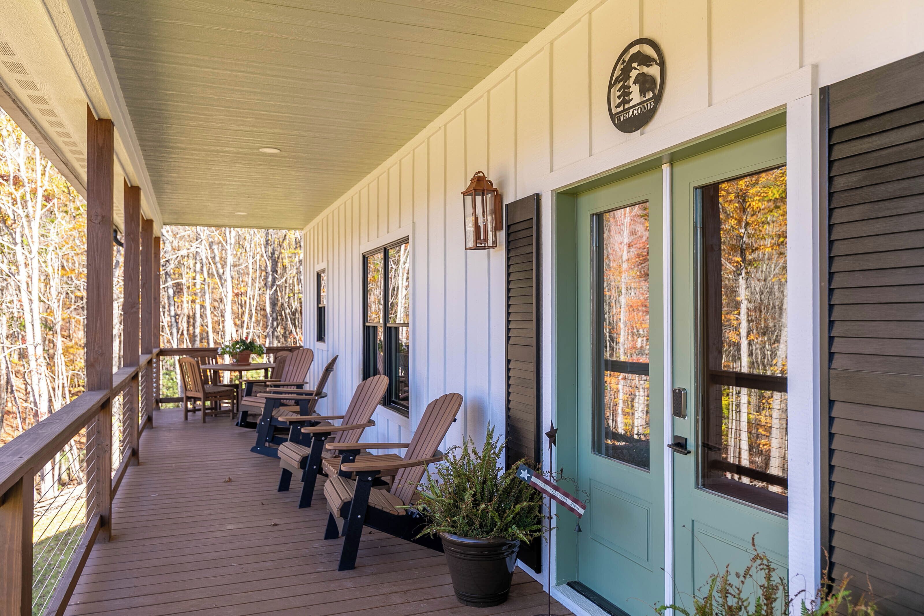 A covered porch with wooden chairs and a table, a green door, and a sign above the door.