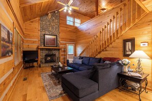 A cozy log cabin interior with a fireplace, wooden staircase, and comfortable seating area. - 4J Getaway (Boone)