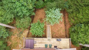 A wooden deck with a built-in bench and two chairs, surrounded by dense greenery. - 4J Getaway (Boone)