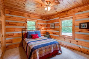 A log cabin bedroom with a bed, two windows, a ceiling fan, and a framed picture on the wall. - 4J Getaway (Boone)