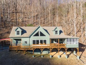 Eine zweistöckige Blockhütte mit Veranda und Deck, umgeben von einem Wald.