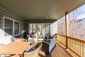 A covered porch with wicker furniture, a wooden table, and a glass door leading to a deck. - Mountain View Retreat (Banner Elk)