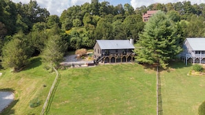A large house with a covered porch and a stone fireplace, surrounded by a well-maintained lawn and dense trees. - Horse Valley Lodge (Boone)