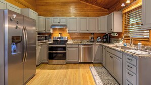 A modern kitchen with stainless steel appliances, white cabinets, and a wooden ceiling. - Horse Valley Lodge (Boone)