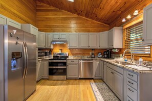 A modern kitchen with stainless steel appliances, white cabinets, and a wooden ceiling. - Horse Valley Lodge (Boone)