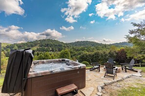 A hot tub with a wooden bench and two Adirondack chairs in a garden setting with a view of a forested hill. - Horse Valley Lodge (Boone)