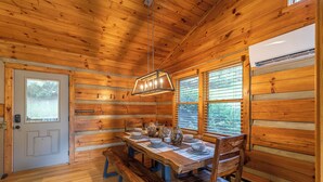 A wooden cabin interior with a dining table set for four, benches, and a hanging light fixture. - Horse Valley Lodge (Boone)